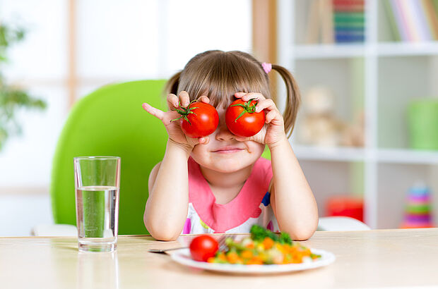 Junges Mädchen am Tisch hält sich Tomaten vor die Augen.