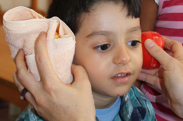 Junge hält eine Eieruhr in ein Handtuch gewickelt an sein Ohr.
