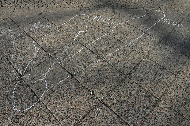 Auf dem Boden sind Kreidemarkierungen vom Schattenwurf dreier Kinder gezeichnet.