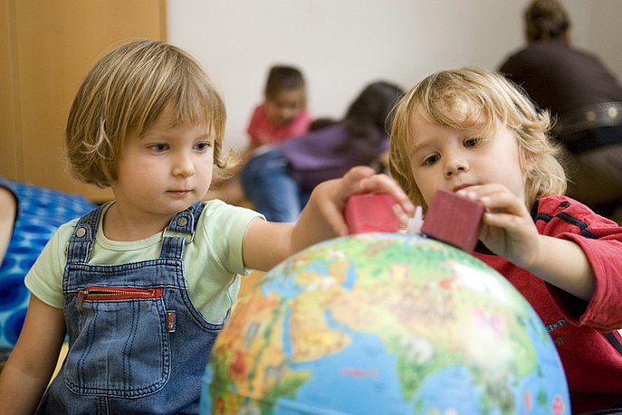 Junge und Mädchen aus der Kita berühren einen Globus.
