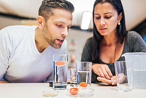 Ein Mann und eine Frau forschen mit Sprudelgas in zwei Wassergläsern.