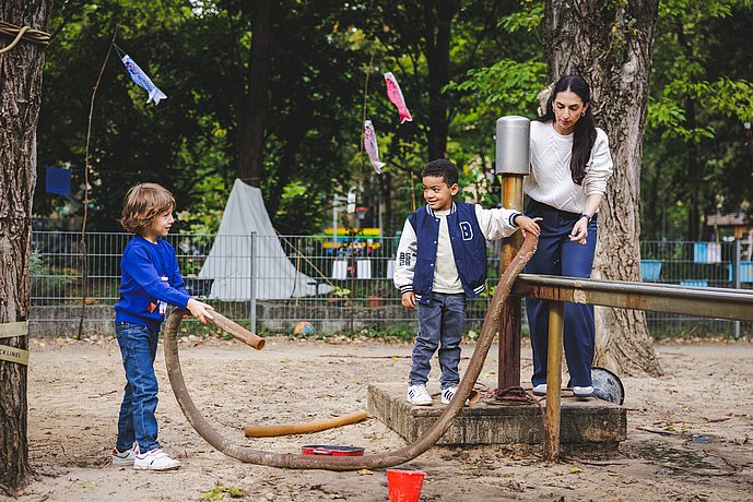 Kinder experimentieren mit einem Wasserschlauch im Kitagarten
