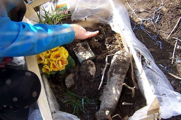 Kind befüllt eine Holzkiste mit Erde und Pflanzen.