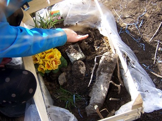 Kind befüllt eine Holzkiste mit Erde und Pflanzen.