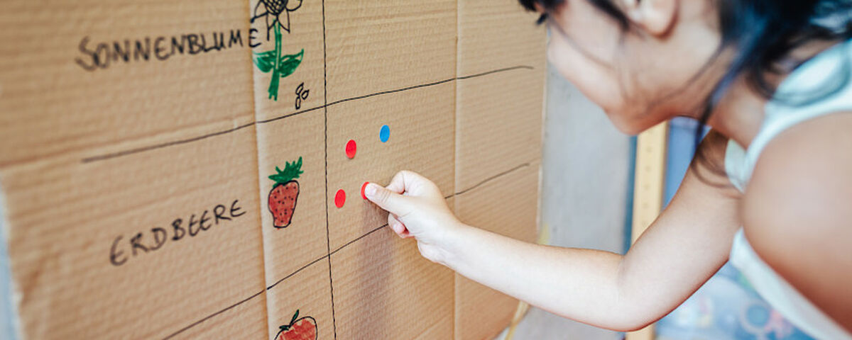 Ein Mädchen klebt rote Punkte auf einen selbstgebastelten Saisonkalender.