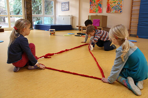 Kinder stecken ein Dreieck auf dem Boden ab.