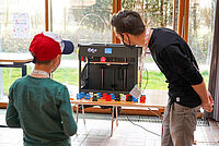 Ein Mann und ein Junge schauen, wie der 3D-Drucker einen Bären produziert.