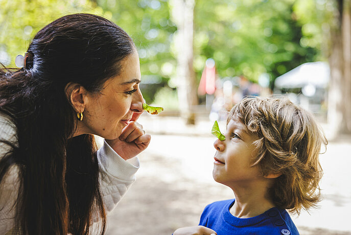 Eine Frau zeigt einem Kind ein Ahronblat auf der Nase
