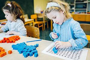 Ein Mädchen experimentiert mit Baussteinen und einem Bauplan mit Zahlen.