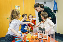 Erzieherin gemeinsam mit fünf Kindern an einem Tisch voller Experimentiermaterialien