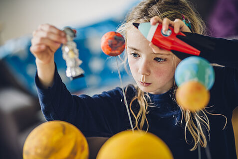 Ein Mädchen schaut konzentriert auf gebastelte Planeten.