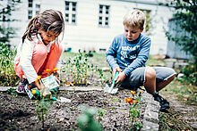 Ein Mädchen und ein Junge vergraben eine Tetrapackung im Gartenbeet