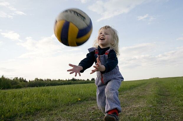Kleines Mädchen fängt einen Volleyball auf.