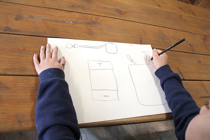Kind zeichnet eine Batterie auf ein weißes Papierblatt