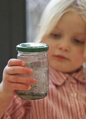 Ein Mädchen hält beobachtend ein Glas mit schmutzigem Wasser