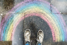 Zwei Schuhe stehen vor einem mit Kreide auf den Boden gemalten Regenbogen