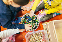 Kinder greifen in eine Schüssel mit Murmeln und Hülsenfrüchten