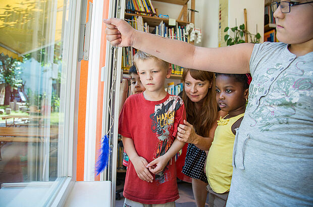 Kinder halten einen Faden mit leichten Feder vor ein Fenster.