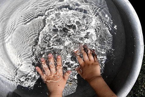 Ein Kind planscht mit den Händen in einem Wasserbecken.